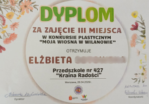Na zdjęciu widoczny jest dyplom za zajęcie III miejsca w konkursie plastycznym „Moja Wiosna w Wilanowie”, przyznany dziecku z Przedszkola nr 427 „Kraina Radości”.