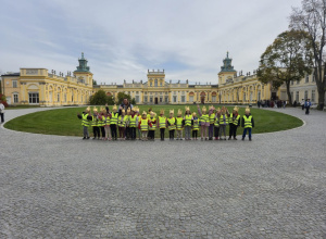 Przedszkolaki w odblaskowych kamizelkach i papierowych koronach przed Pałacem w Wilanowie.