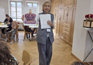 Edukatorka muzealna prezentuje dzieciom ilustrację bursztynowej królewskiej korony podczas zajęć edukacyjnych