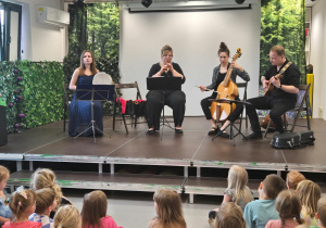 Dzieci oglądają koncert na żywo, podczas którego czworo muzyków gra na różnych instrumentach.