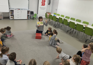 Grupa dzieci siedzących w kręgu w sali bibliotecznej, uczestnicząc w zajęciach bibliotecznych.