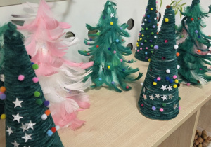 Świąteczne choinki wykonane przez dzieci podczas przedszkolnych warsztatów plastycznych, ozdobione piórkami, pomponami i gwiazdkami.