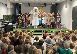 Dzieci biorące udział w przedszkolnym przedstawieniu teatralnym, występujące na scenie w bajkowych kostiumach aniołów i postaci z opowieści.