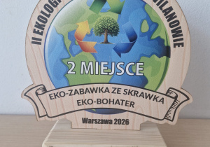 Drewniana statuetka z motywem Ziemi i recyklingu, przyznana za zajęcie 2 miejsca w wydarzeniu „II Ekologiczny Kwiecień w Wilanowie” za konkurs „Eko-zabawka ze skrawka - Eko-bohater” (Warszawa 2026).