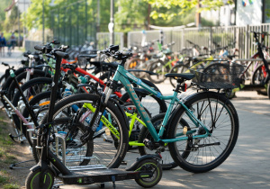 Stojaki rowerowe z licznymi rowerami i hulajnogami zaparkowanymi przed placówką.