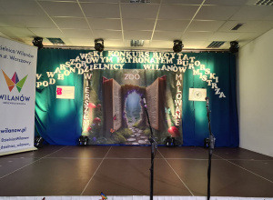 Scena Warszawskiego Konkursu Recytatorskiego pod patronatem Burmistrza Dzielnicy Wilanów, ozdobiona bajkową scenografią z motywem otwartej księgi i mikrofonami dla uczestników w
