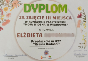 Na zdjęciu widoczny jest dyplom za zajęcie III miejsca w konkursie plastycznym „Moja Wiosna w Wilanowie”, przyznany dziecku z Przedszkola nr 427 „Kraina Radości”.
