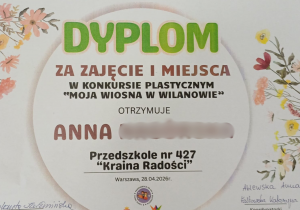 Na zdjęciu widoczny jest dyplom za zajęcie I miejsca w konkursie plastycznym „Moja Wiosna w Wilanowie”, przyznany dziecku z Przedszkola nr 427 „Kraina Radości”.