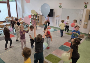 Dzieci bawią się kolorowymi balonami podczas wspólnej zabawy ruchowej w sali przedszkolnej.