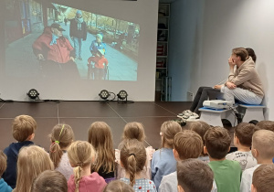 Dzieci oglądają prezentację dotyczącą codziennych sytuacji i funkcjonowania osób z niepełnosprawnością ruchową.