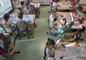 Dzieci przy stolikach wykonują kolorowe prace plastyczne przedstawiające jesienne liście.