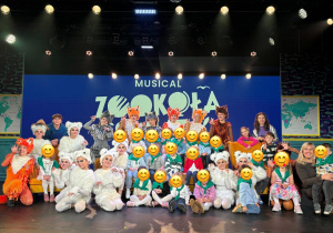 Pamiątkowe zdjęcie przedszkolaków z aktorami w kostiumach zwierząt na scenie po musicalu „ZOOkoła świata"